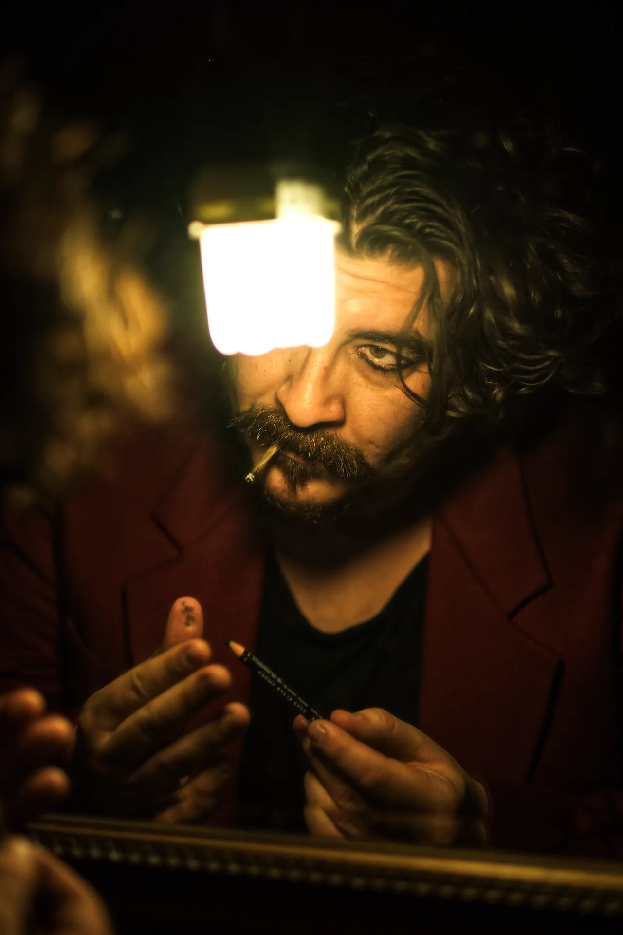 Uomo con barba e capelli ricci illuminato da una lanterna, una sigaretta tra le labbra, luce calda