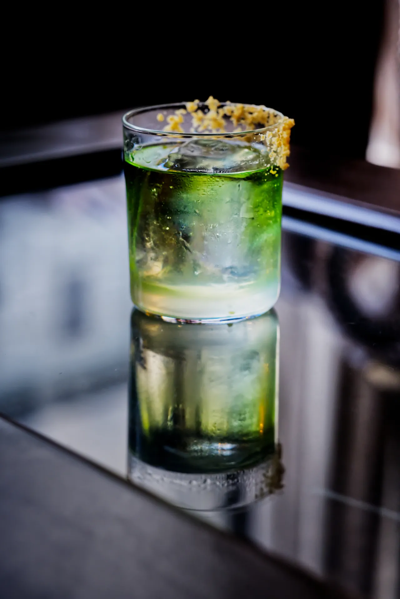 Cocktail verde con bordo di agrumi riflesso su un bancone a specchio