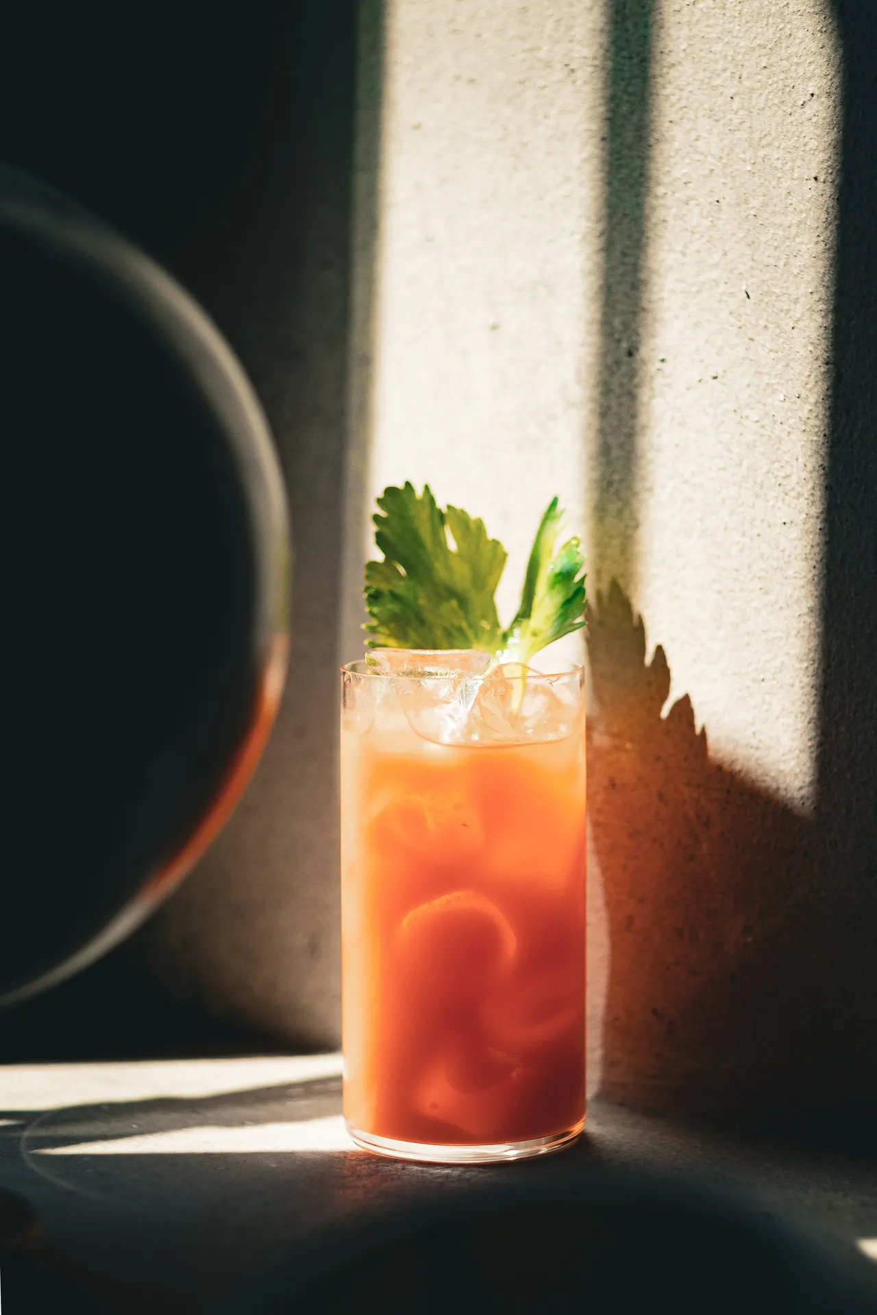 Highball arancio con sedano in una lama di luce, accanto a una sfera di vetro