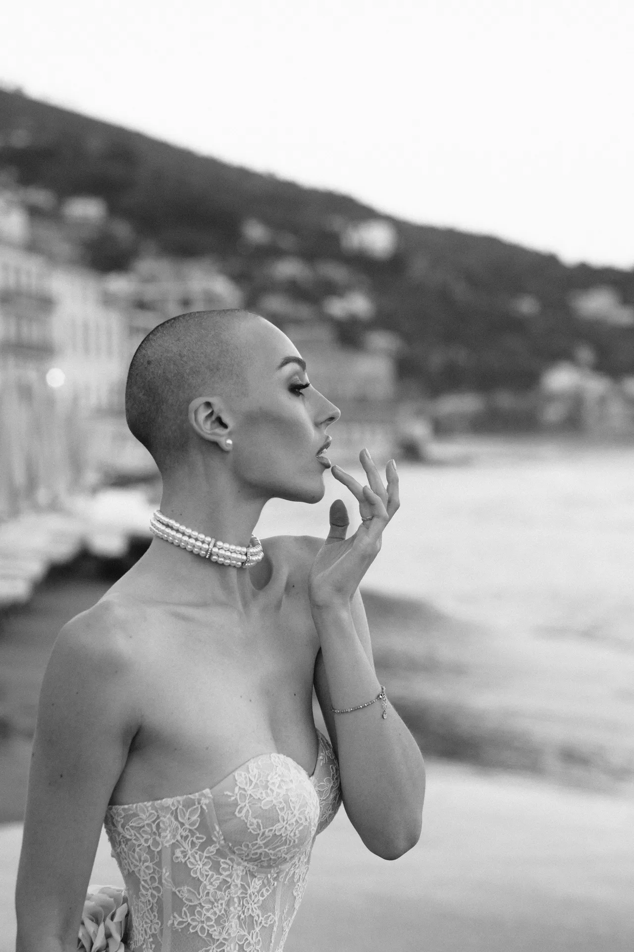 Profilo di donna con collana di perle e abito in pizzo, sullo sfondo la costa sfocata