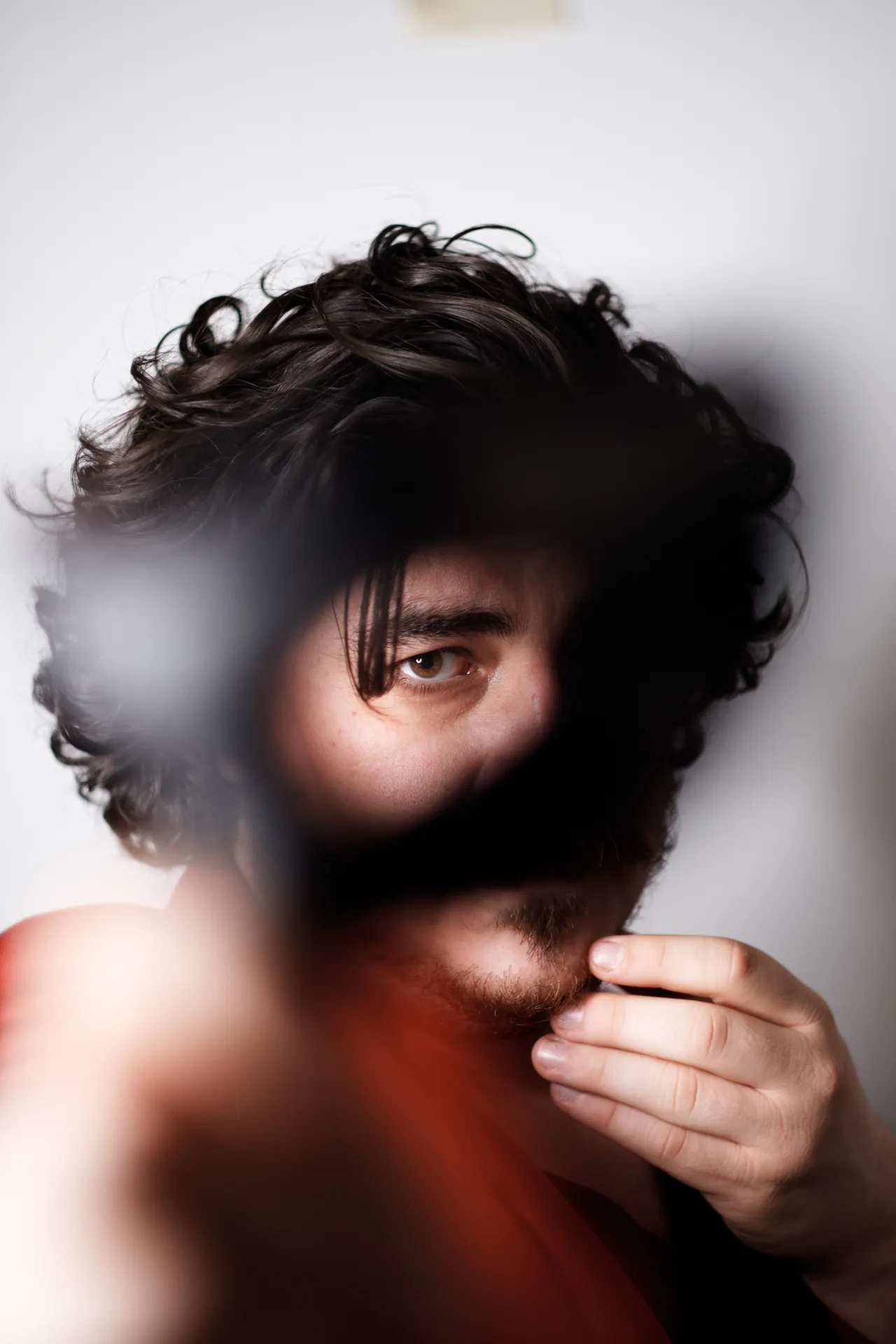 Volto di uomo dai capelli ricci che guarda oltre un oggetto sfocato in primo piano