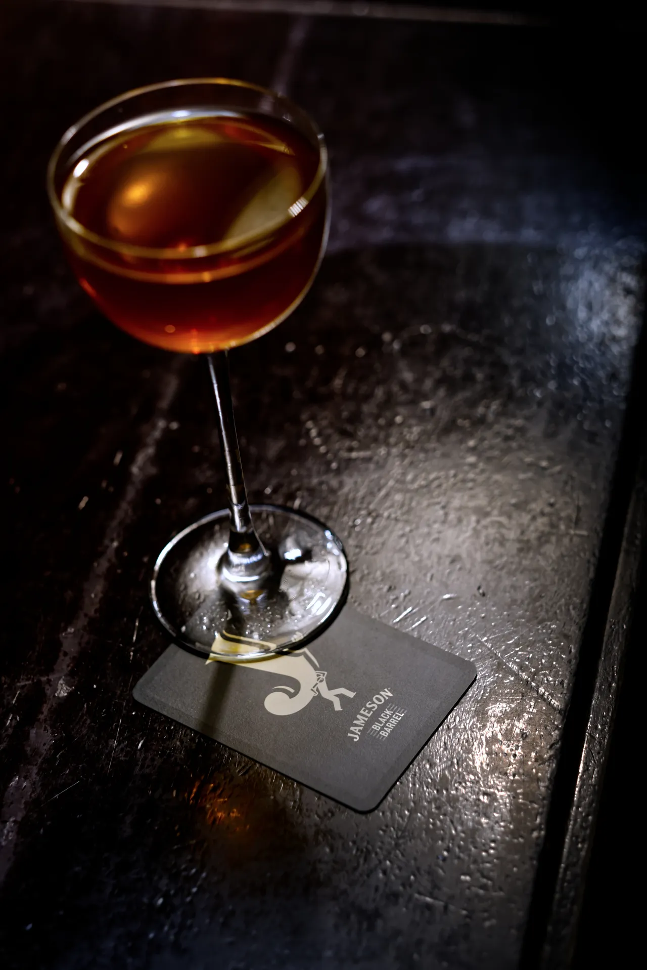 Cocktail ambrato in coppa su un sottobicchiere, su un tavolo di legno scuro