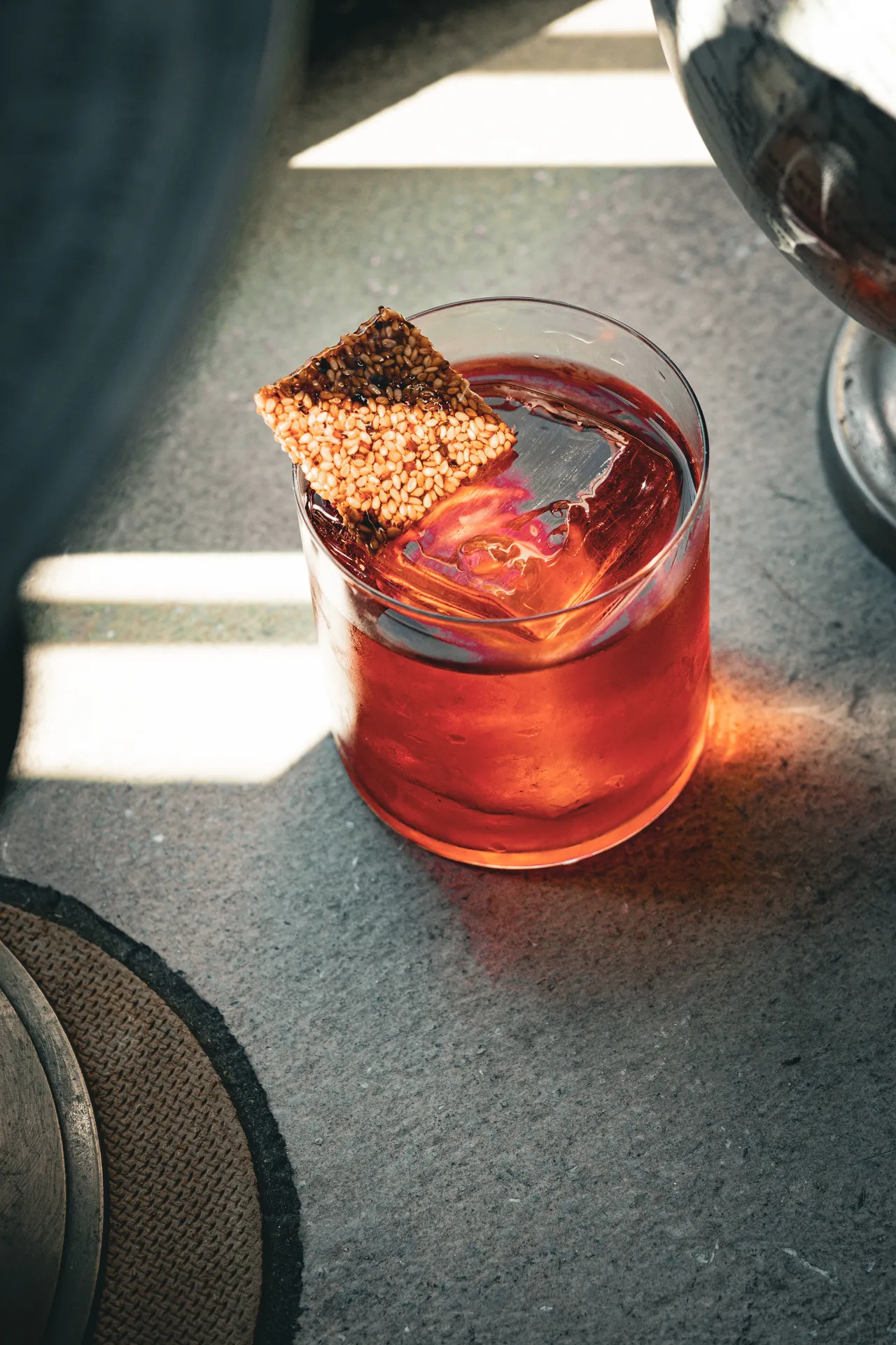 Tumbler con cocktail rosso e una cialda croccante, luce di finestra su cemento