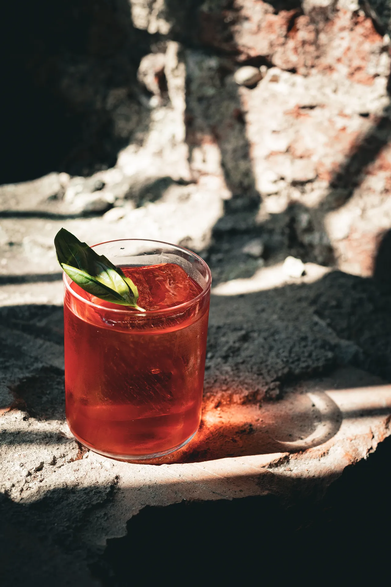 Cocktail rosso con foglia verde su un muro grezzo in pietra e mattoni