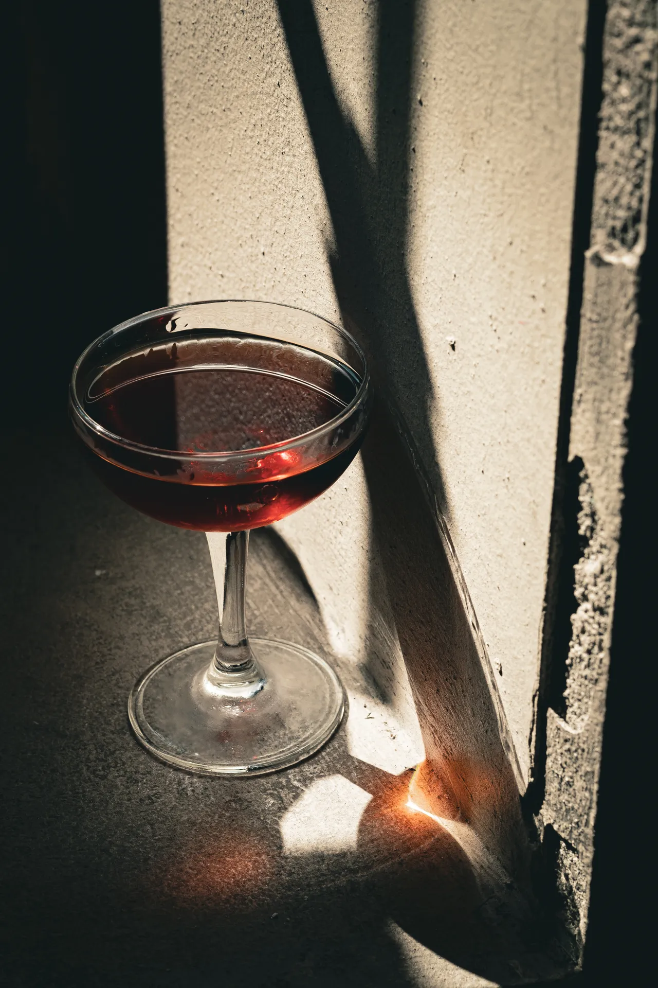 Coppa con drink rosso tagliata da ombre diagonali su cemento