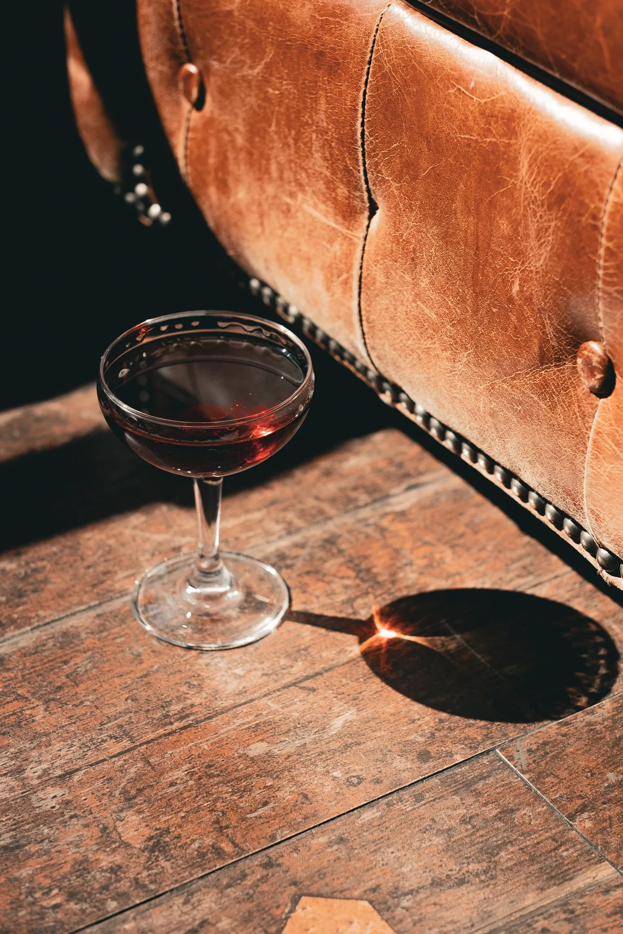 Coupette con drink ambrato sul parquet accanto a un divano chesterfield in pelle