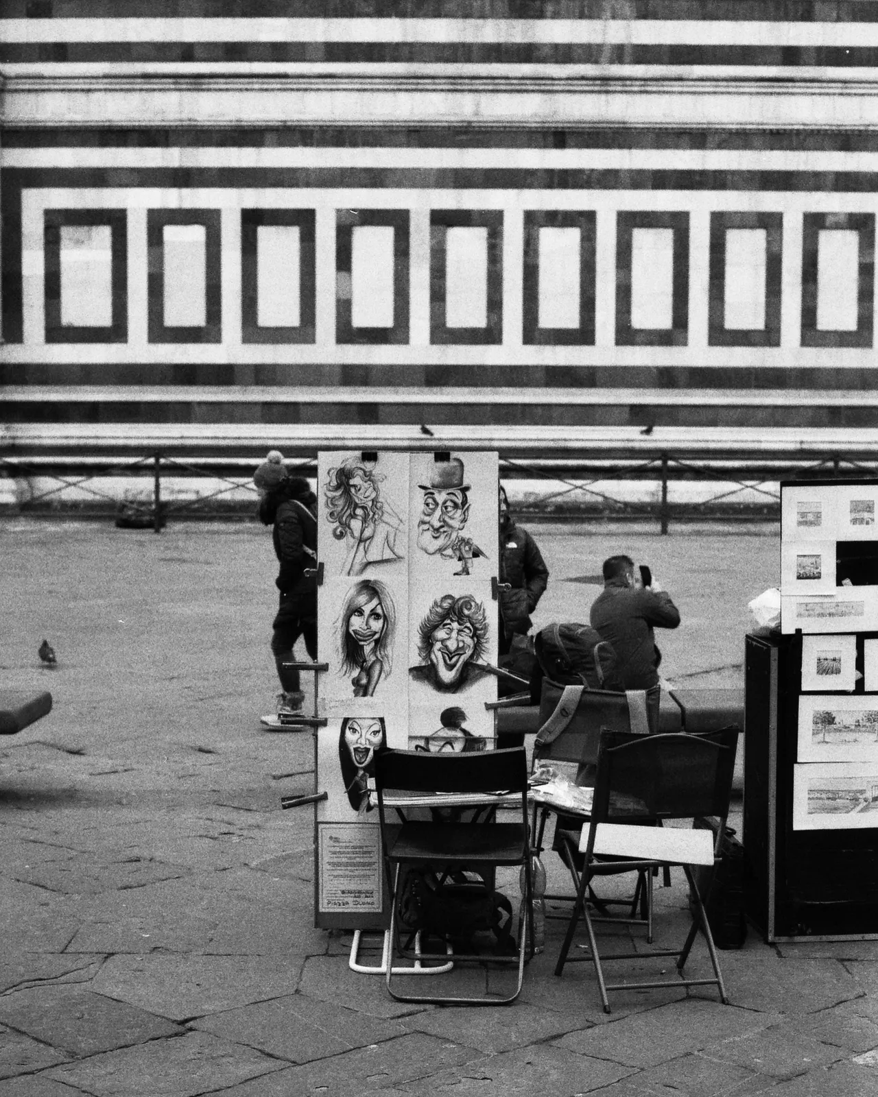 Banco di un caricaturista davanti ai marmi bianchi e verdi del Duomo di Firenze