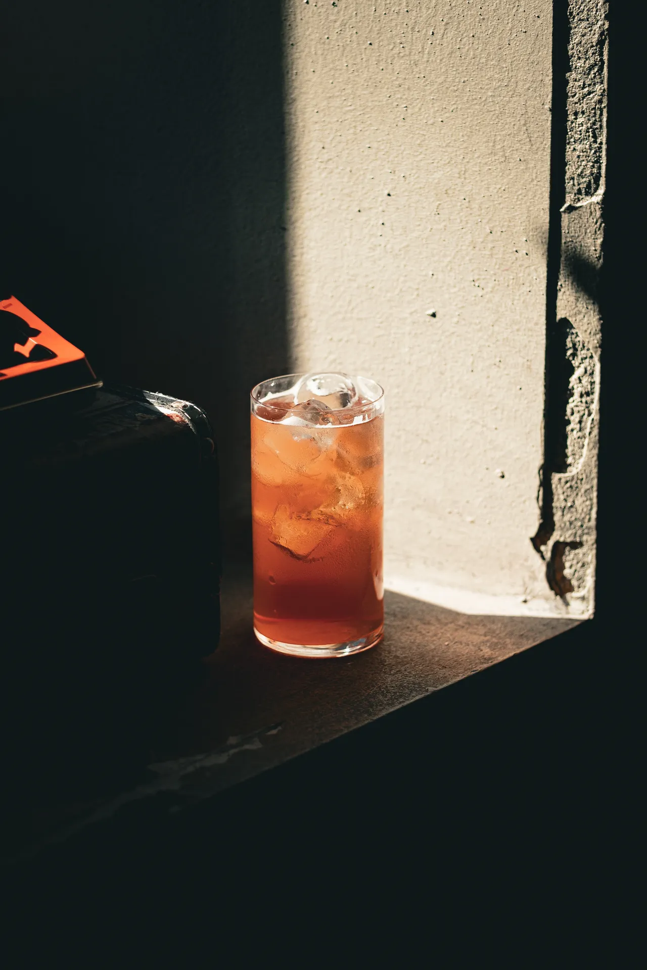 Highball arancio con ghiaccio sul davanzale, metà in luce e metà in ombra