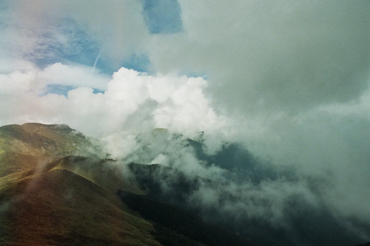 Crinali di montagna verdi tra nuvole basse e cielo azzurro